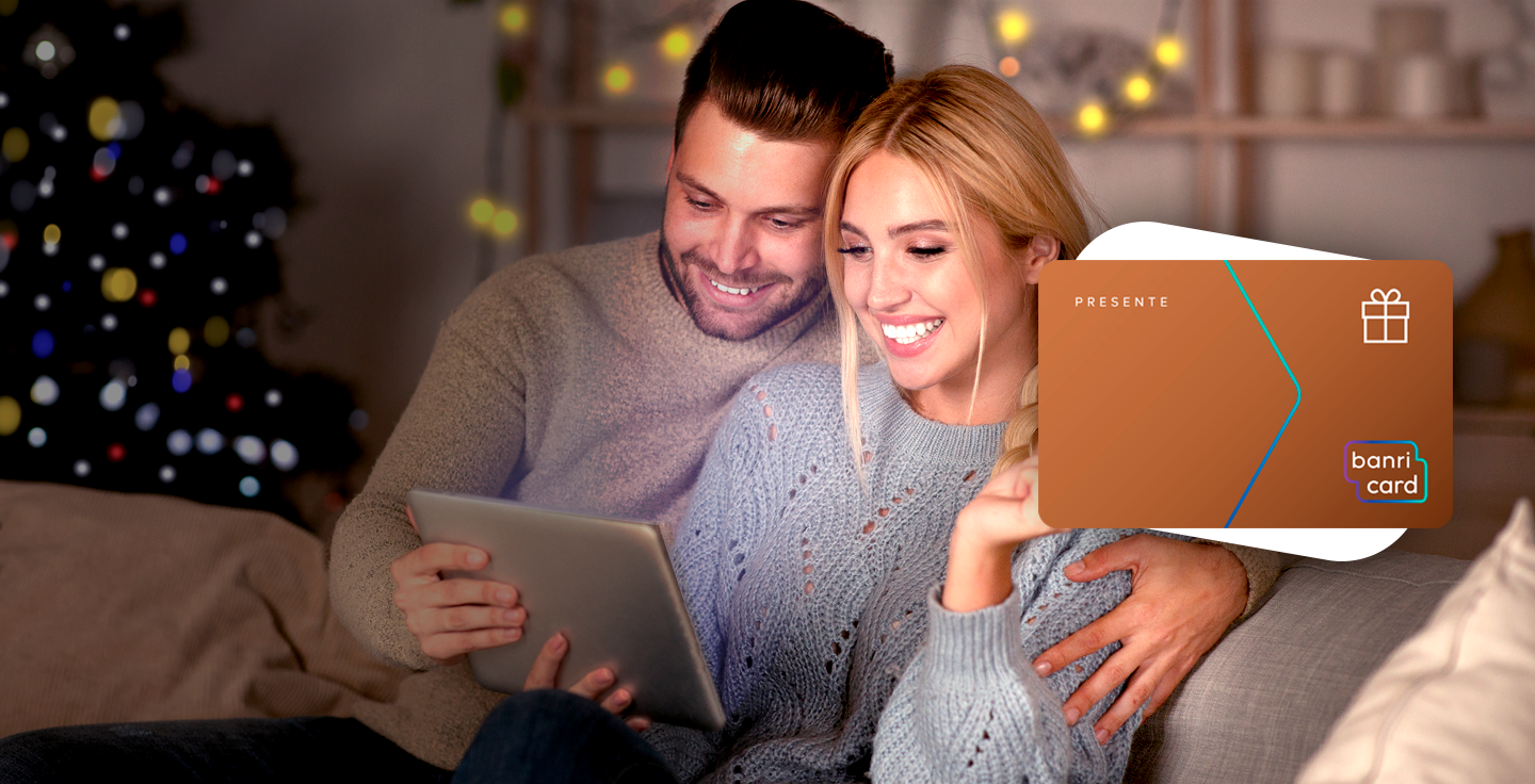 Foto de casal de homem e mulher sorrindo enquanto olham a tela do tablet. A imagem do carto BanriCard Pagamentos est em primeiro plano.